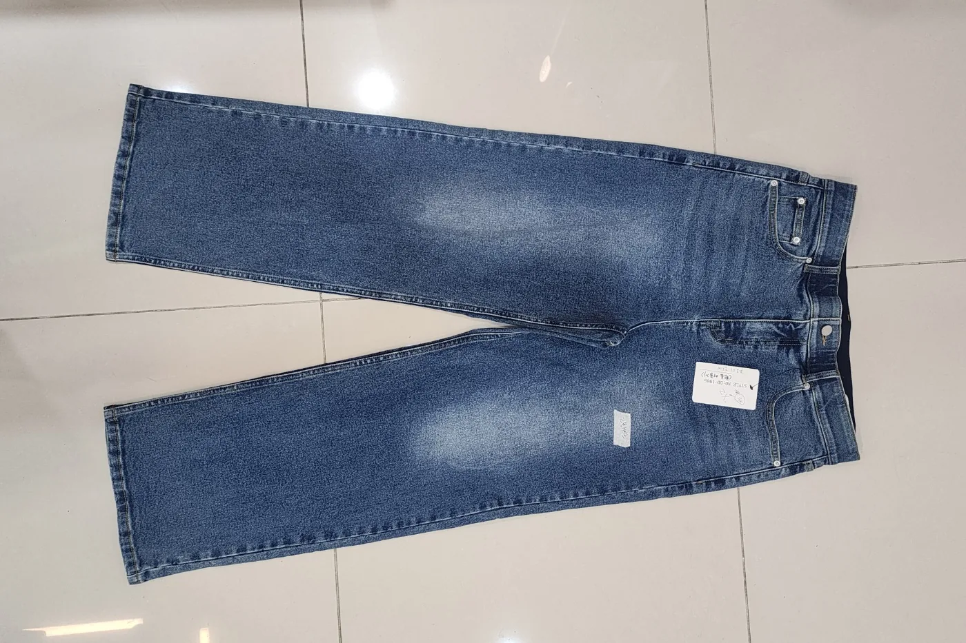 A denim jeans sample from a plus-size project, laid flat on a tiled floor