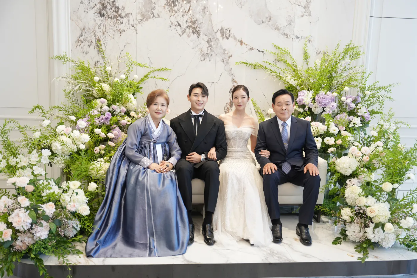 양가 부모님과 신랑 신부가 꽃 장식 앞에 나란히 앉은 원판 사진